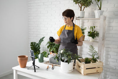 Side view of woman holding potted plant against wall