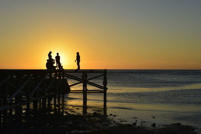 Silhouette people on beach against sky during sunset