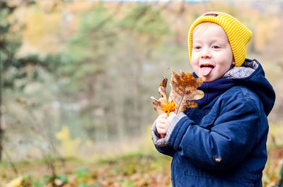 A little cheerful boy collects yellow leaves in the autumn forest.