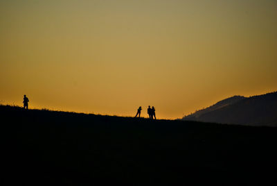 Silhouette people on land against clear sky during sunset