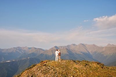Rear view of people standing on mountain against sky