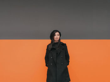 Young woman looking away against orange wall