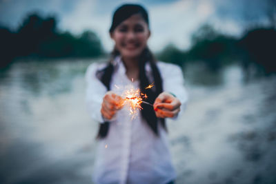 Young woman holding sparkler at night