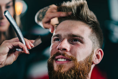 Close-up of woman shaving man beard