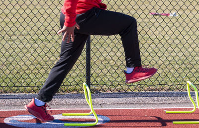 Track runner standing over yellow mini hurdles in the a-position preforming speed training drills.