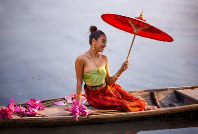 Woman holding umbrella by louts while sitting on boat in lake