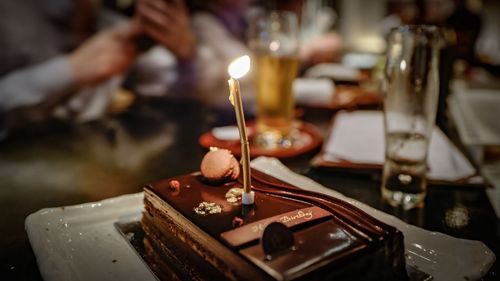 Illuminated candle on birthday cake at table