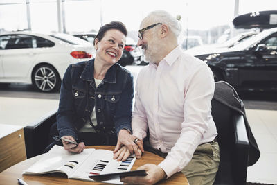 Happy senior couple reading brochure at car showroom