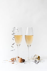 Two glasses of champagne, cork, ribbon and confetti on white backdrop.