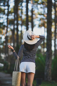 Rear view of woman in hat standing against trees