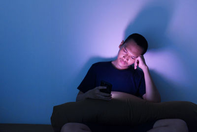 Young woman using mobile phone while sitting on wall