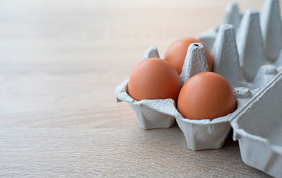 A carton of three fresh red free range eggs on a wooden table