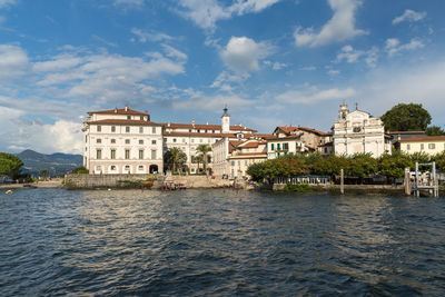 Buildings by river against cloudy sky