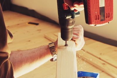 Cropped image of man using power tool on plank