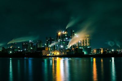 Illuminated city by sea against sky at night