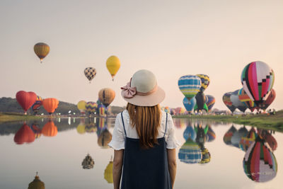 Rear view of woman standing by lake with balloons flying against sky