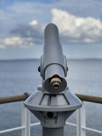Close-up of coin-operated binoculars by sea against sky
