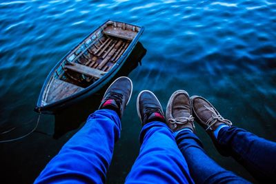 Low section of friends sitting by boat moored at lake