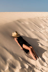 Young female tourist lying down on sandy hill while exploring dunes of corralejo at sundown in fuerteventura canary islands spain