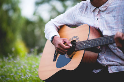 Midsection of man playing guitar in park