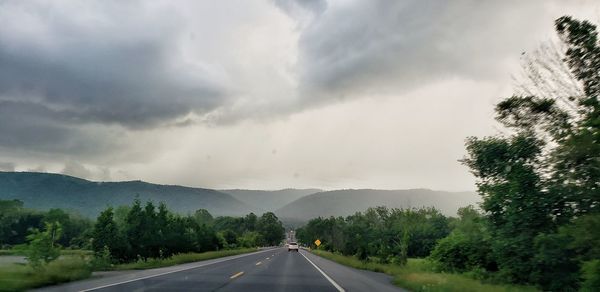 Road by trees against sky