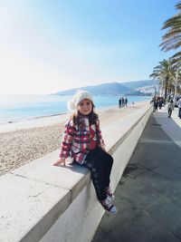 Full length portrait of girl sitting on retaining wall