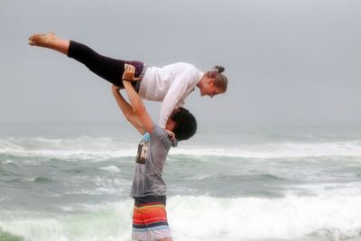 Man carrying woman at beach against sky