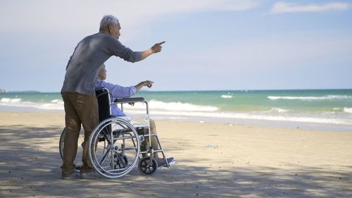 Asian back elderly woman disabled sit in wheelchair and husband is a wheelchair user on the beach