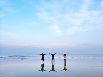 Rear view of people on wet beach by sea against sky