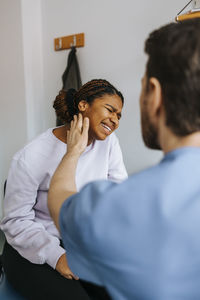 Male medical professional checking anxious patient's neck ache in examination room