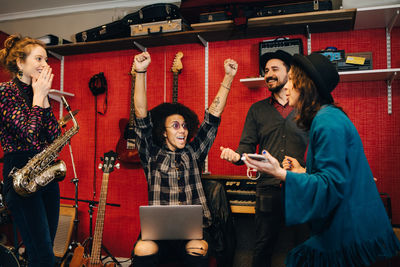 Male and female friends celebrating while standing against instruments at recording studio