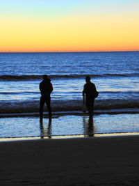 Silhouette people on beach against sunset sky