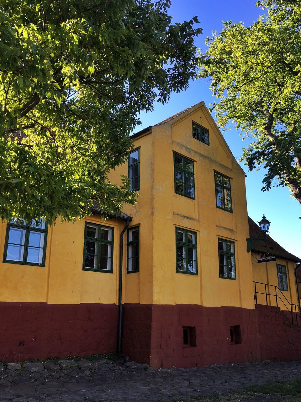 building exterior, architecture, built structure, tree, yellow, window, residential building, residential structure, house, clear sky, building, day, facade, sunlight, outdoors, no people, growth, sky, shadow, low angle view