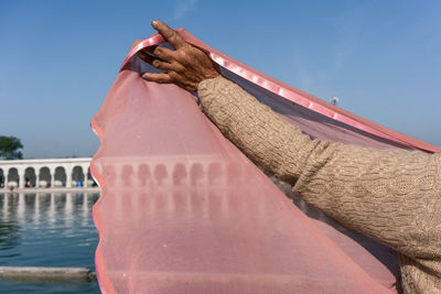 Close-up of woman holding pink veil against clear blue sky