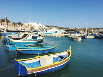 Boats moored at harbor against clear blue sky