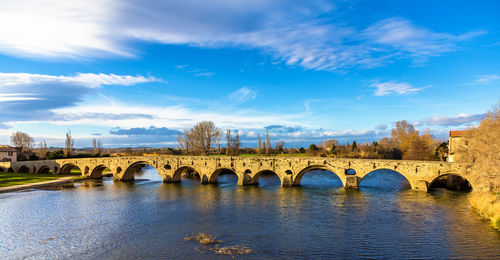 Arch bridge over river against cloudy sky