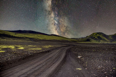 Dirt road amidst landscape against sky at night
