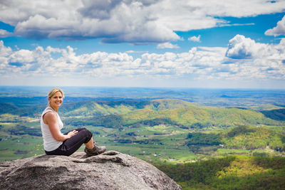 Full length of woman sitting on rock against sky