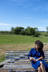 Side view of woman sitting on field against sky