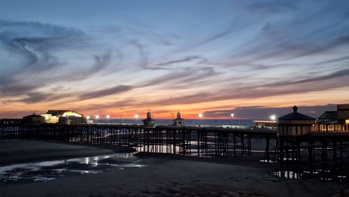 Illuminated pier over the sea against sky during sunset