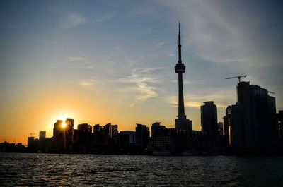 View of skyscrapers by river against sky during sunset