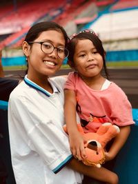 Portrait of smiling teenage girl carrying sister while standing outdoors