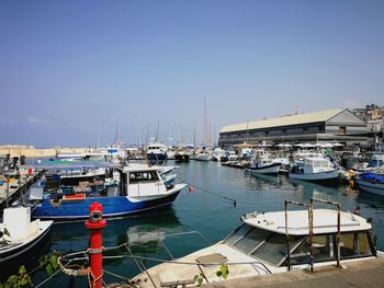 Boats moored at harbor against clear blue sky