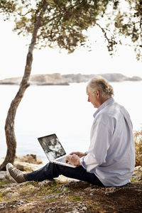 Senior man using laptop outdoors on picnic