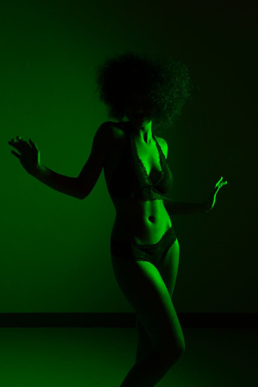 one person, indoors, studio shot, green color, adult, women, dancing, standing, young adult, human arm, three quarter length, beauty, fashion, illuminated, limb, front view, females, arms raised, beautiful woman, hairstyle, body part, human limb, nightlife