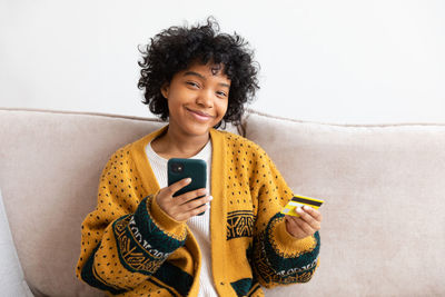 Young woman using mobile phone while sitting on sofa at home