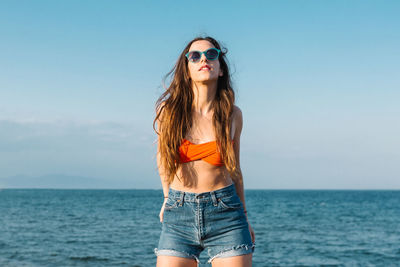 Portrait of young woman wearing sunglasses against sea against sky