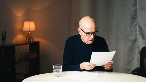 Elderly man sitting at the table reads his electricity and gas bills