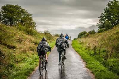 Rear view of people riding bicycle on country road