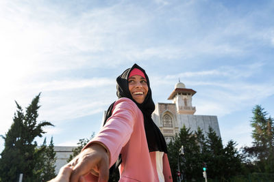 Portrait of smiling woman holding camera against sky